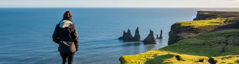 En person på Dyrhólaey med utsikt over Reynisdrangar og Atlanterhavet.