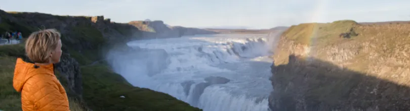 En person i oransje jakke ser ut over fossen Gullfoss.