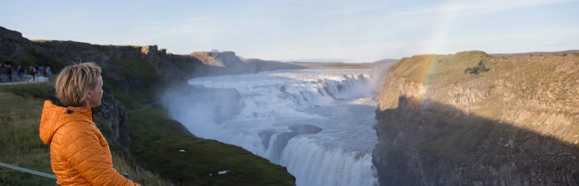 En person i oransje jakke ser ut over fossen Gullfoss.