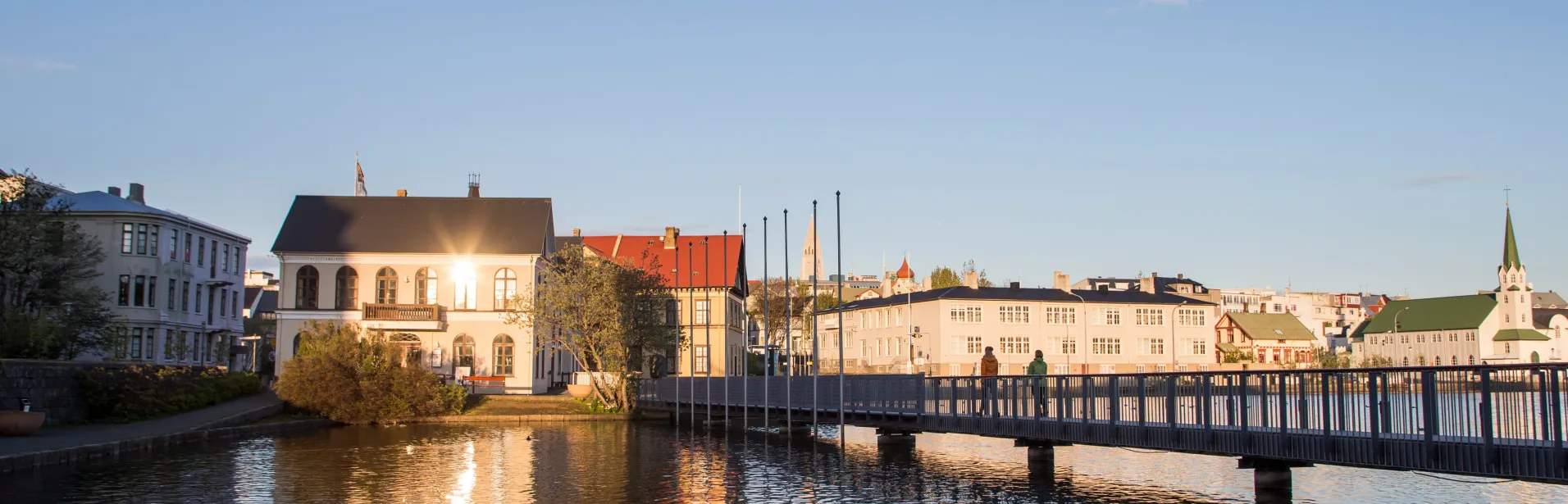 Hus og en gangbro ved Tjörnin i Reykjavík i kveldslys.